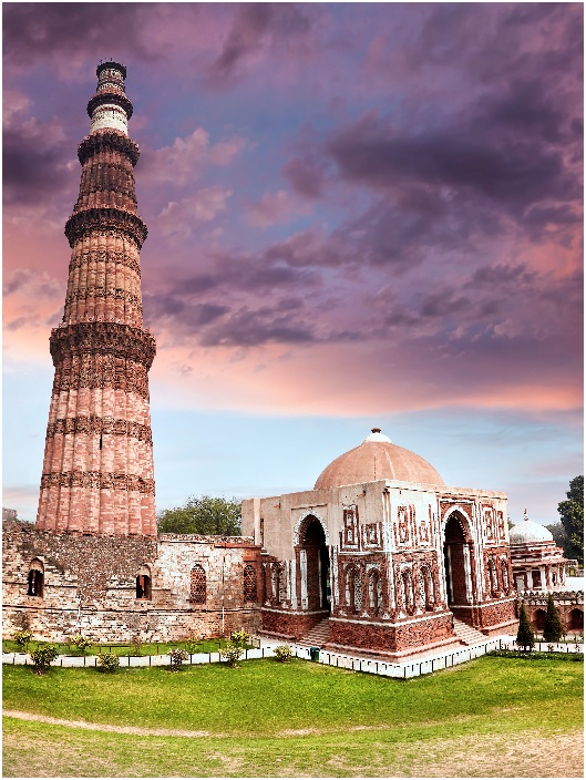 Big Tower and ruined wall at Qutub Minar complex in New Delhi, India at purple sunset